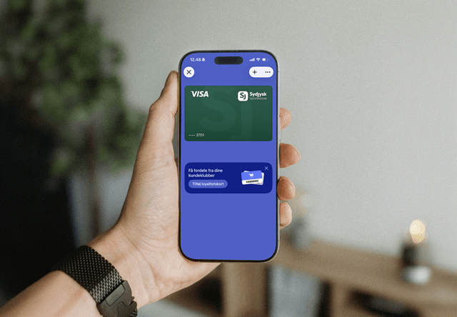 Billede at en hånd der holder en mobiltelefon hvor man kan de Sydjysk Sparekasse Visakort