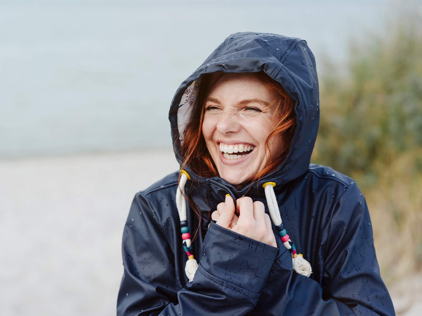 Dame i mørkeblå regnjakke smiler på en strand