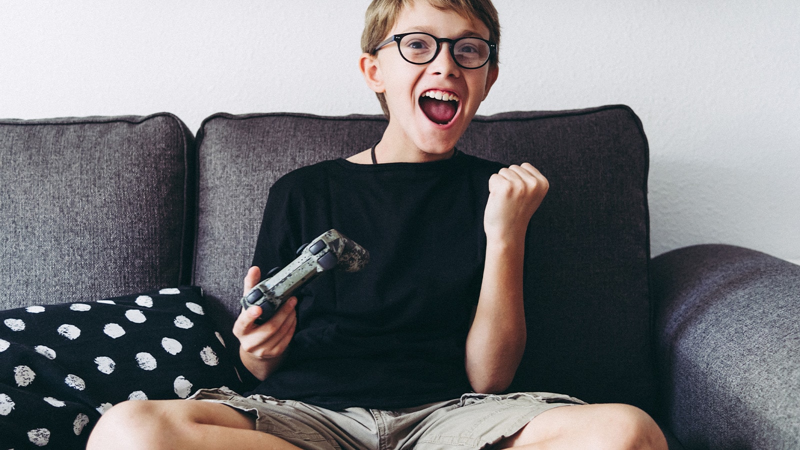 Barn spiller videospil med controller i sofa.