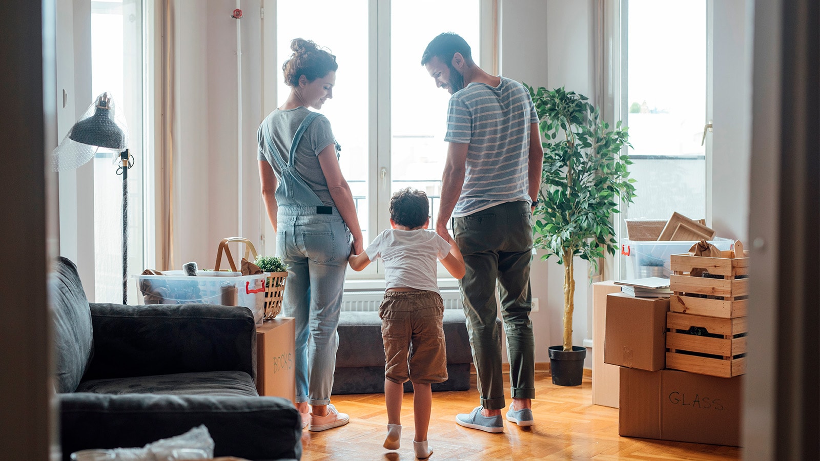 Familie på 3 holder i hånd i deres hjem med front mod vindue