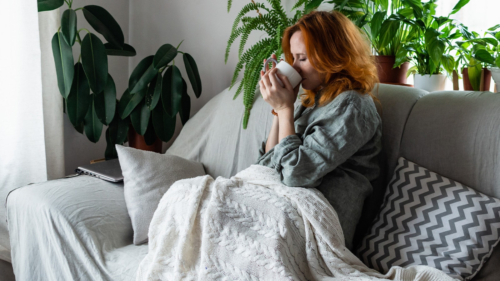 Kvinde sidder i sofa med en kop te