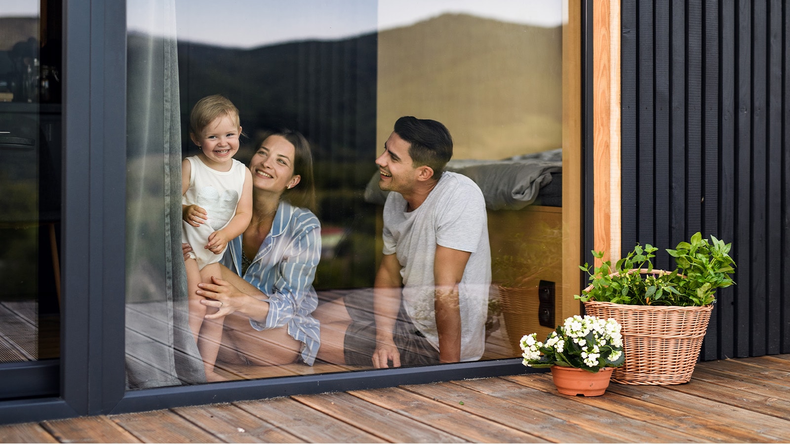 Familie bag rude hvor mor og far sidder på gulvet og barnert står op og kigger ud med smil på læben