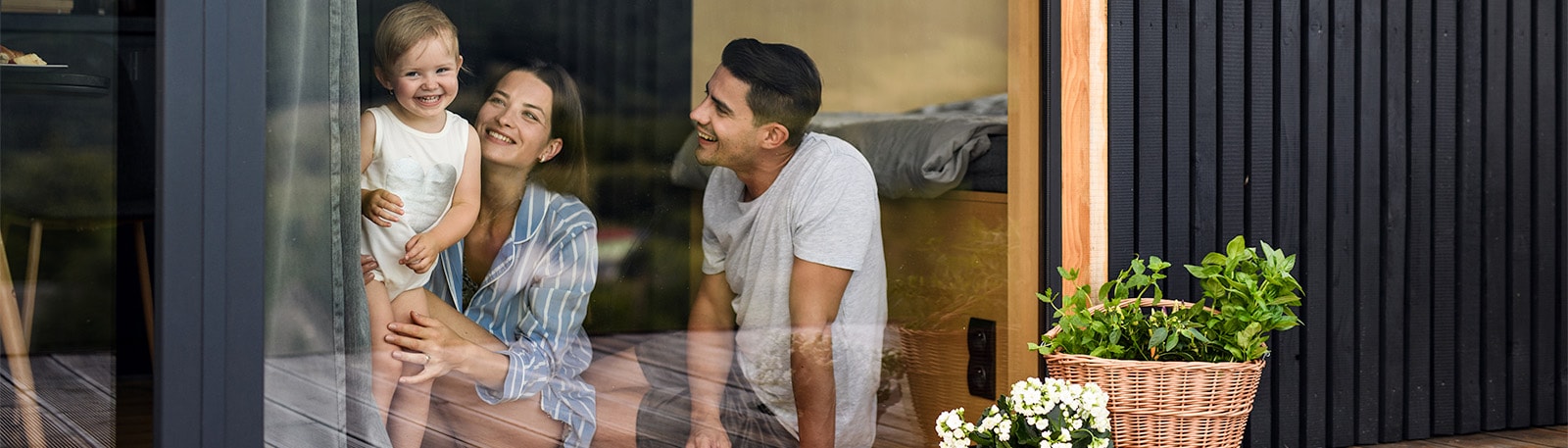 Familie bag rude hvor mor og far sidder på gulvet og barnert står op og kigger ud med smil på læben