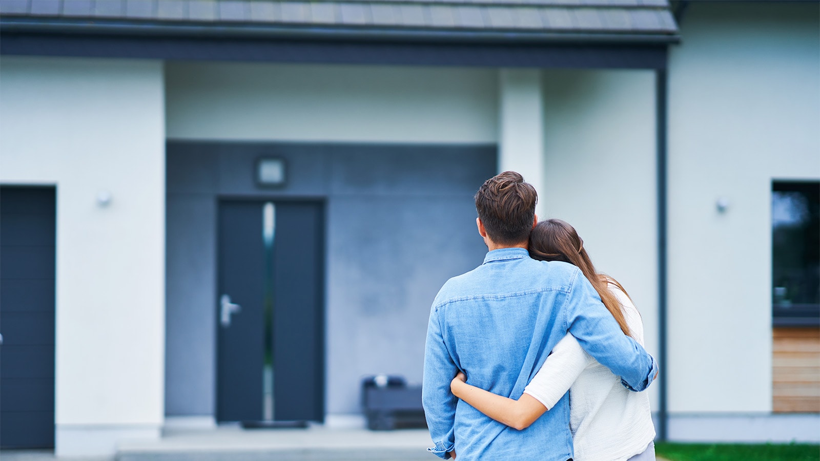 Par foran hus kigger på deres hjem med armene om hinanden