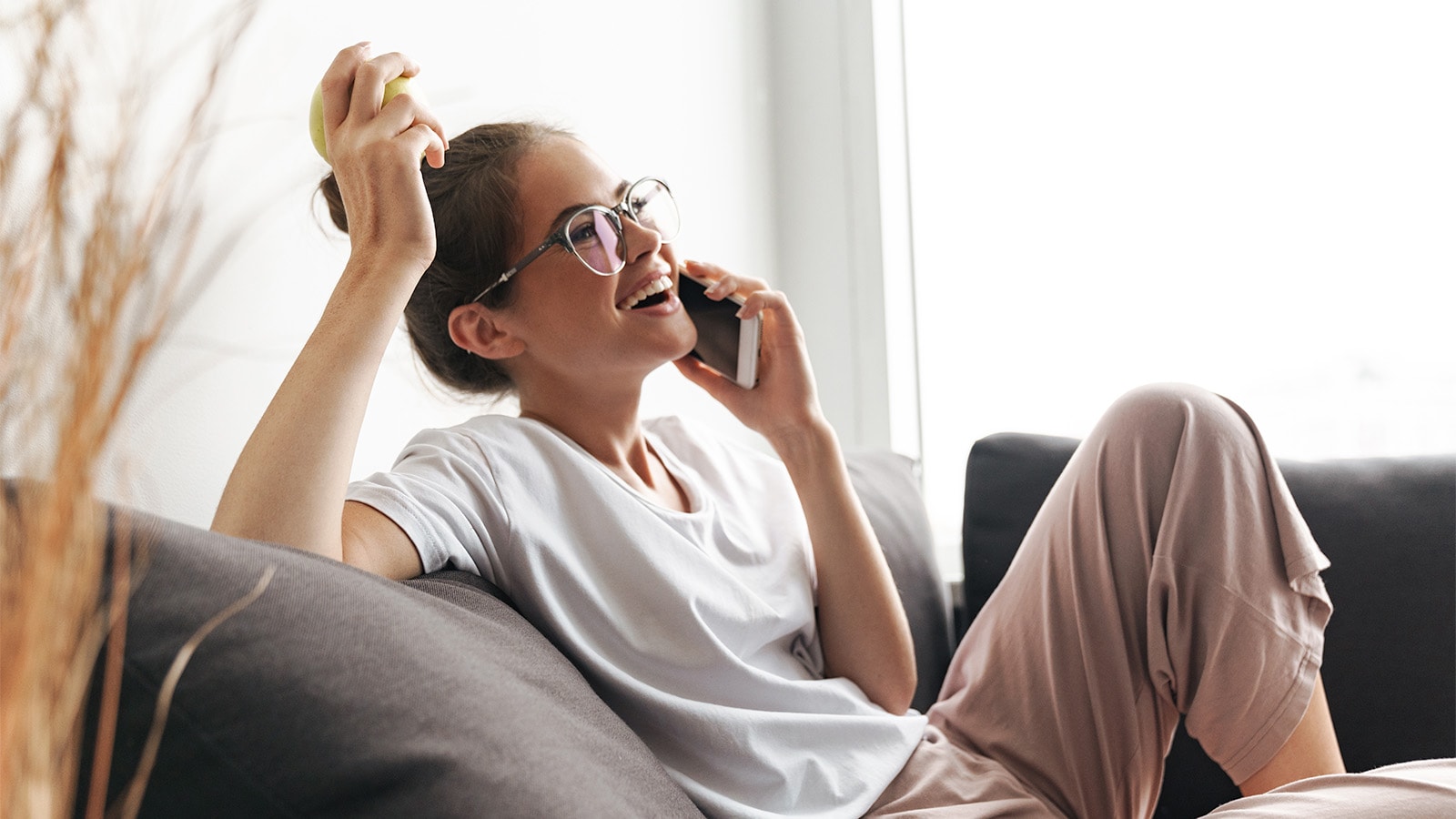 Ung pige i sofa med mobiltelefon og æble i hånden 