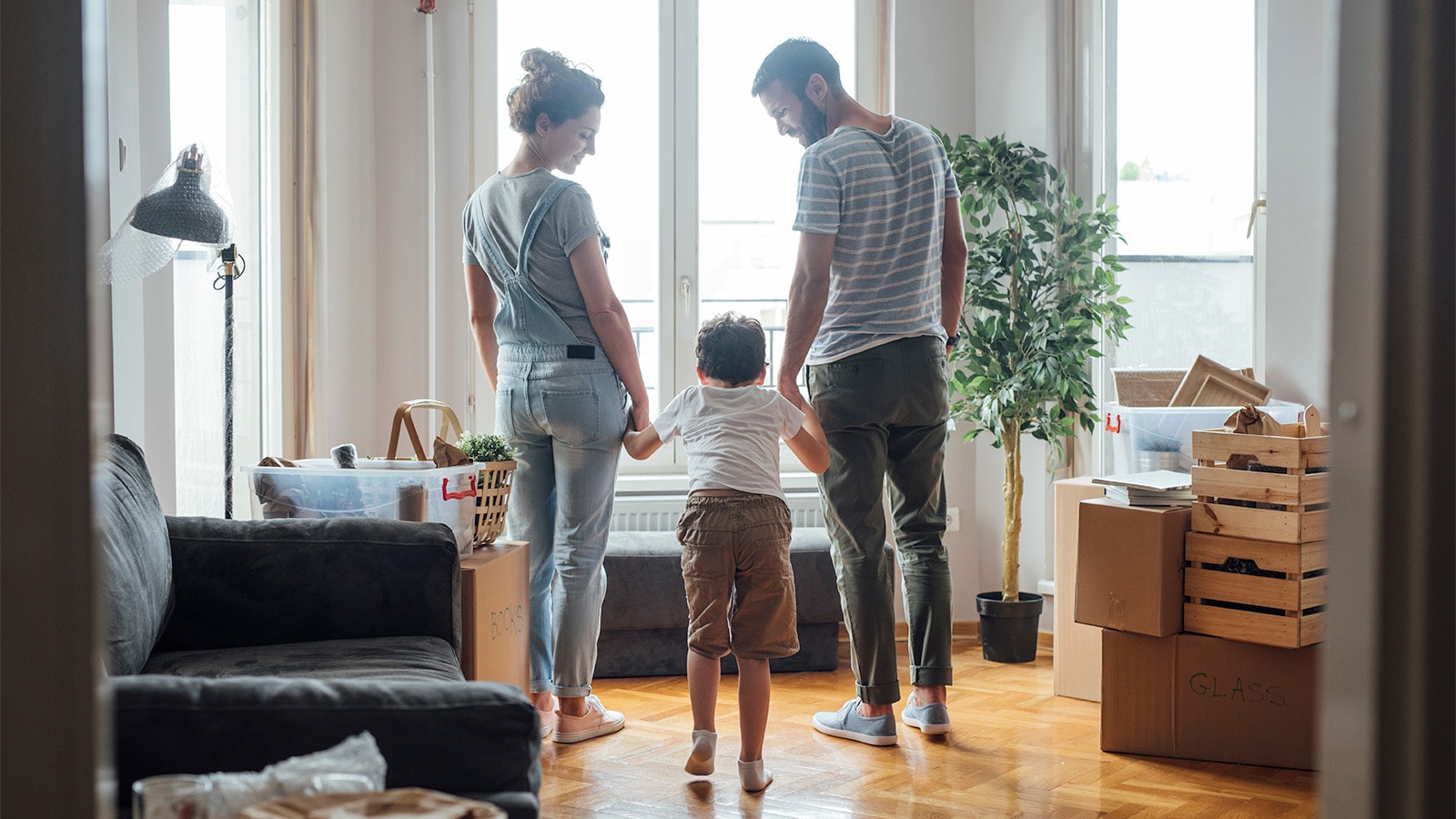 Familie på 3 holder i hånd i deres hjem med front mod vindue