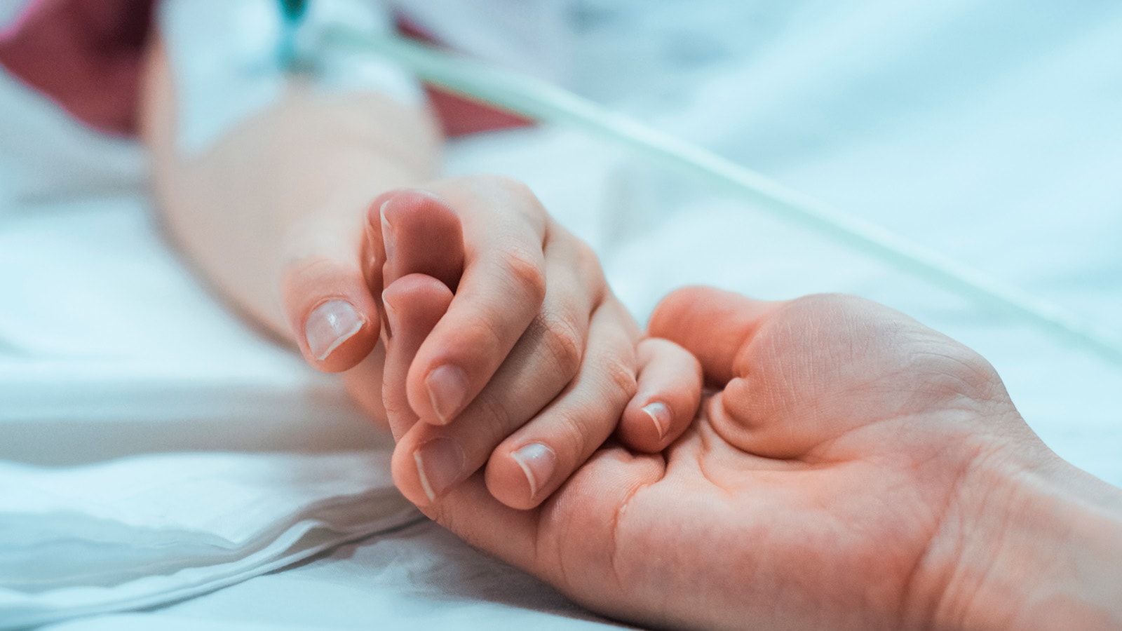 2 voksne hænder holder i hånd. den ene er syg og ligger i sygeseng med drop