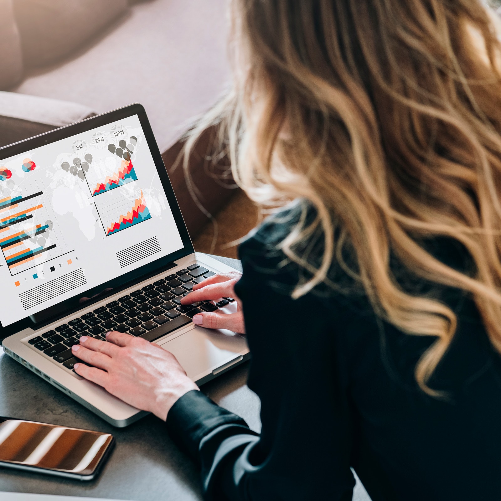 Dame foran sin bærbar med diagrammer på. Hendes mobil ligger ved siden af.