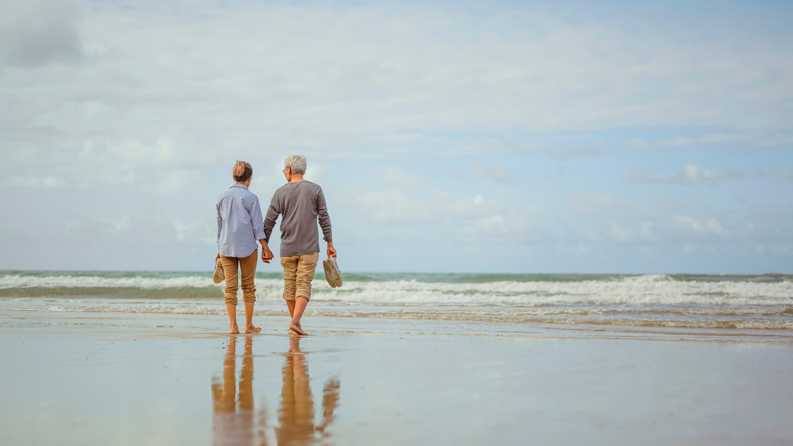 2 pensionister går på stranden med fødderne i havet