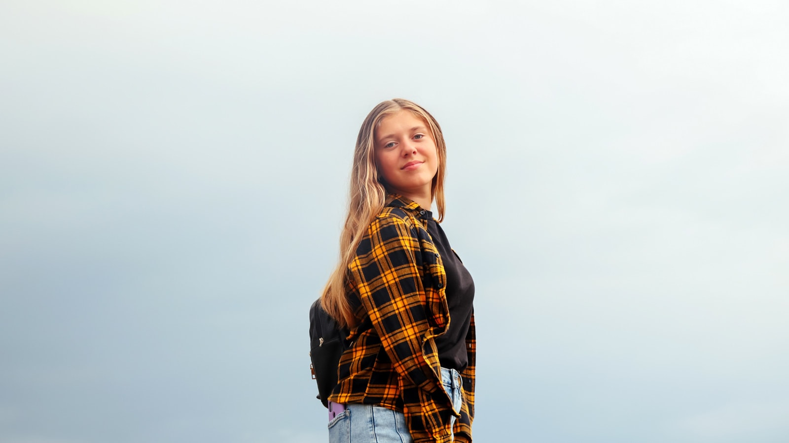 Pige-teenager poserer med siden til og smiler til kameraet med blåligt baggrund