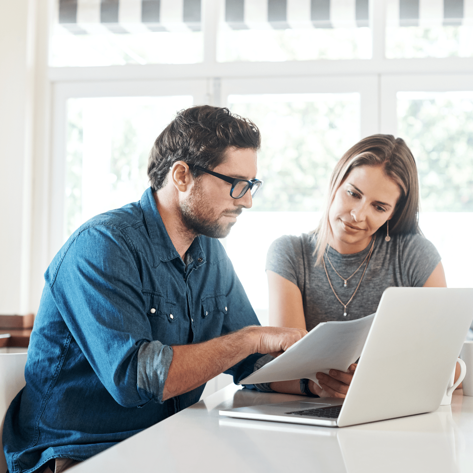 Et par sidder ved bordet og kigger på nogle papirer med deres bærbar åben